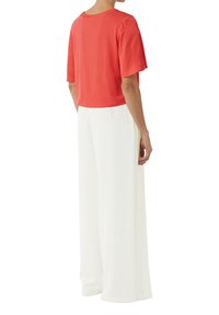 Koraalkleurig t-shirt met korte mouwen, gecombineerd met witte wijde broek. Het shirt heeft een ronde halslijn en een relaxte pasvorm, terwijl de broek soepel en vloeiend valt.