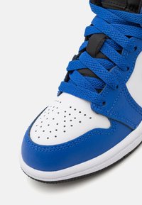 Blue and white sneaker with a smooth leather upper, perforated toe box, and flat laces. Black accents at the tongue and eyelets.