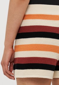 Strikkede shorts i flerfargede striper av oransje, rød, svart, krem og beige; teksturert stoff med en litt ribbet overflate.