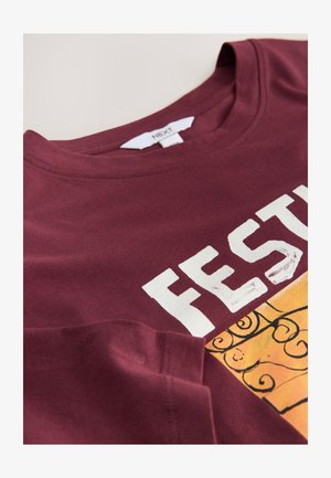 Burgundské bavlněné tričko s velkým bílým nápisem "FEST" a barevným designem s dekorativním vzorem scroll na spodní části.