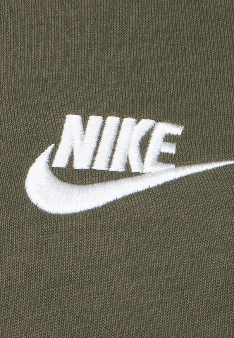 Tissu vert olive avec un logo Nike brodé en blanc, incluant un swoosh sous le nom de la marque, sur fond texturé.