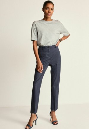 T-shirt grigio a maniche corte abbinato a pantaloni a vita alta a righe blu scuri. Il modello indossa sandali con tacco blu, con le mani sui fianchi.