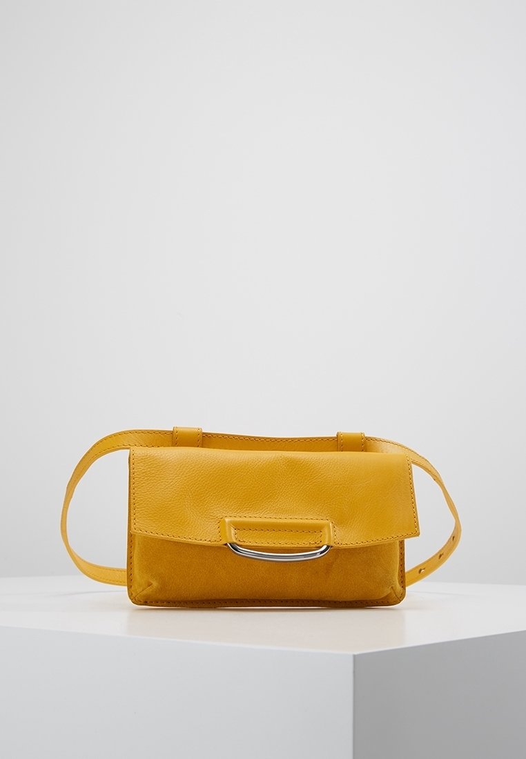 Petit sac à main en cuir jaune moutarde avec fermeture à rabat et détail de poignée en métal argenté, exposé sur un socle blanc sur un fond uni.