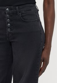 Čierne džínsy s vysokým pásom vyrobené z denimu, s piatimi gombíkmi vpredu, bočnými vreckami a rovnými nohavicami.