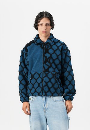 Fleece jacket featuring a blue base with a textured black geometric pattern, zip closure, and side pockets. Soft, cozy feel.