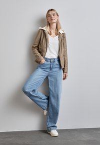 Giacca in ecopelle color beige con cappuccio crema, maglietta bianca e jeans a gamba larga blu chiaro, abbinati a sneakers bianche. Design semplice, look casual.