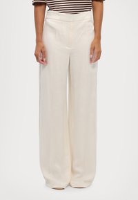 Wijd uitlopende broek van crèmekleurige stof, met voorplooien, hoge taille en subtiele accentnaden aan de zijkant. Gladde textuur en minimalistisch ontwerp.