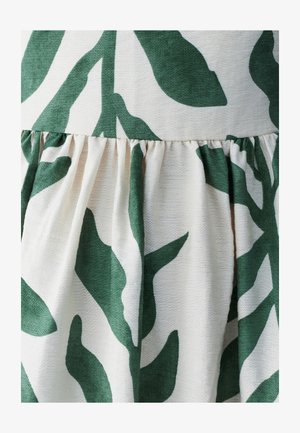 Kangas kukkakuvioilla, jossa suuria vihreitä lehtiä vaaleankermanvärisellä taustalla. Teksturoitu materiaali, jossa on poimutettu yksityiskohtahelma.