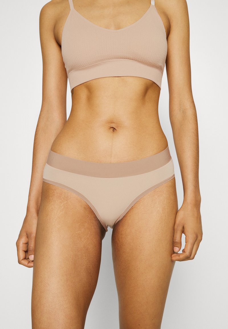 Vaaleanruskea bralette ja siihen sopivat bikinit, jotka on valmistettu sileästä kankaasta. Mallissa on saumaton muotoilu ja kontrastiväriset nauhat vyötäröllä.