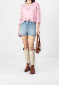 Rosa stickad crop top med öppet mönster, ljusblå denimshorts, beige och bruna knähöga stövlar, brun crossbody-väska.