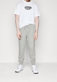 White T-shirt with a black abstract logo, gray sweatpants with a drawstring, and white sneakers with black accents. Simple, casual attire.