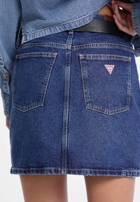 Denim rok in een donkere wassing met achterzakken, een driehoekige logopatch en een licht verbrijzelde zoom. Gepaard met een licht denimjacket.