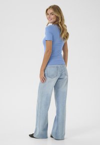 Light blue ribbed short-sleeve top paired with light-wash wide-leg jeans. Top features scalloped hem; jeans show rear pocket detailing.