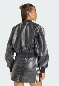 Crna bomber jakna s teksturom krokodilske kože, skraćenog kroja, s rebrastim manšetama i tri bijele pruge koja se protežu niz rukav.