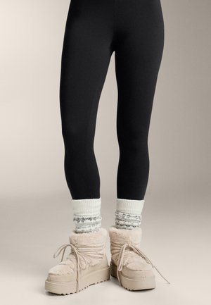 Čierne legíny v kombinácii s krémovými chlpáčovými čižmami s textúrovanou vrchnou časťou, béžovou platformou a pletenými ponožkami so vzorom sivých akcentov.