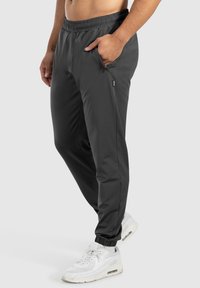 Schwarze, leichte Jogginghosen mit einem elastischen Bund, seitlichem Reißverschlussfach und schmal zulaufenden Bündchen, kombiniert mit weißen Sport Schuhen.