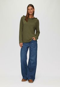Olijfgroene hoodie met lange mouwen, gecombineerd met brede blauwe jeans. Bruine schoenen met gestructureerde zolen maken de outfit compleet.