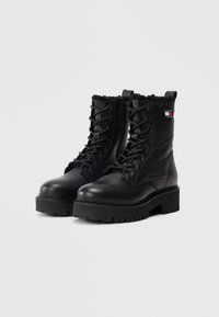 Mustad mustad kõrgbootsid tekstuuriga pinnaga, lipsudega disain, ümar nina, paks platvormi tald ja pehme krae. Omab brändi logo.