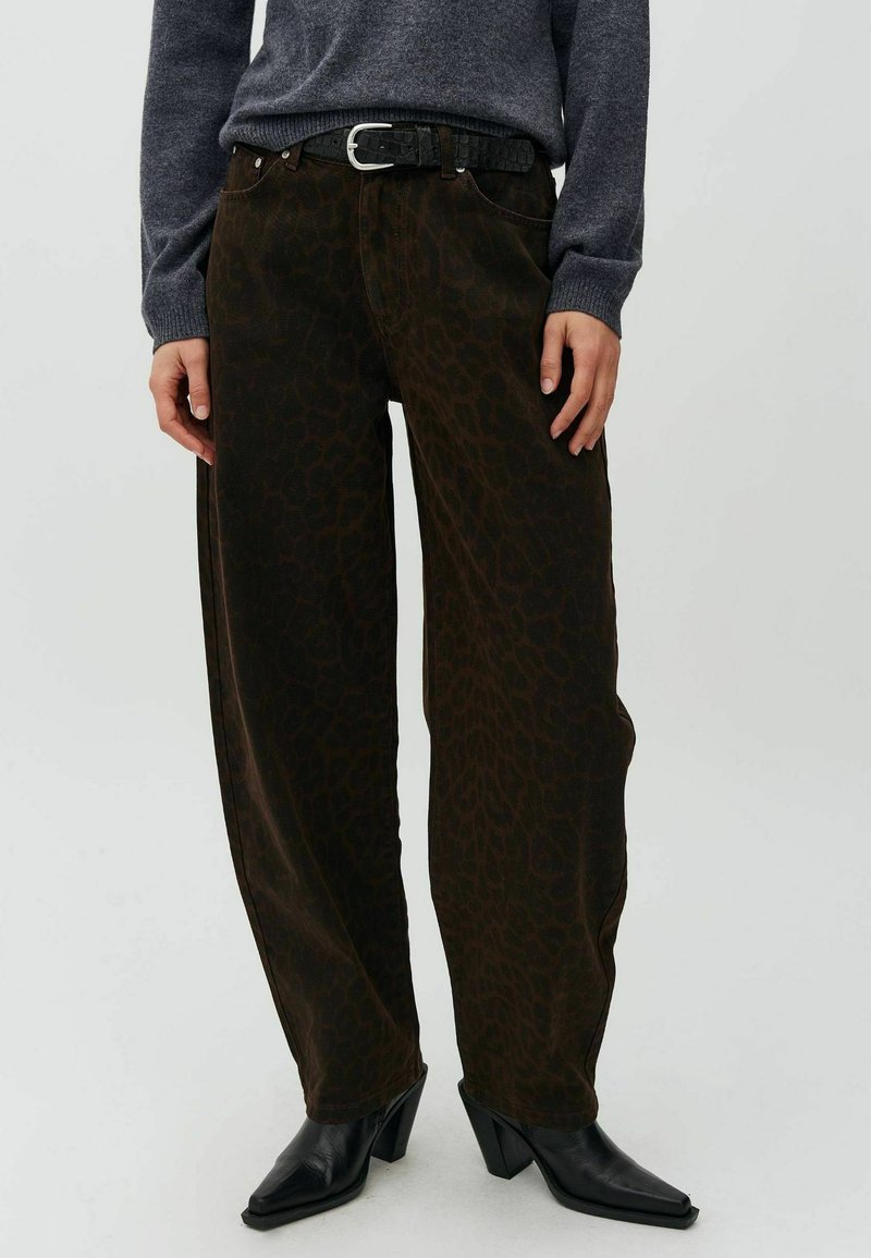 Personne portant un pantalon large marron foncé imprimé léopard, ceinture noire, pull gris foncé et bottines noires à talons.