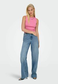 Top senza maniche rosa a coste abbinato a jeans blu a vita alta e gamba larga. L'outfit presenta una texture liscia e una vestibilità casual.