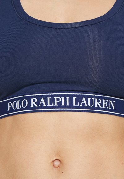 Sportski grudnjak tamnoplave boje s rebrastim uzorkom, širokom elastičnom trakom s bijelim logotipom "POLO RALPH LAUREN" i kontrastnim prugama na donjem dijelu.