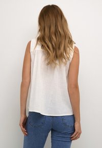 Haut sans manches blanc en tissu texturé, avec un ourlet arrondi et des coutures latérales ; associé à un jean en denim bleu.