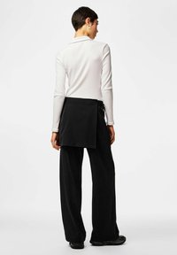 Pantalon large noir associé à un haut blanc à manches longues et côtelé. La tenue présente un design minimaliste et des textures lisses.