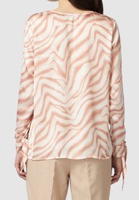 Blusa a maniche lunghe color crema con strisce ondulate rosa. Presenta un collo rotondo e drappeggi alle maniche, realizzata in tessuto morbido.