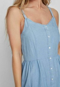 Ljusblå denimklänning med spagettiband, knappstängning framtill och en rynkad midja. Mjuk textur med en avslappnad design.