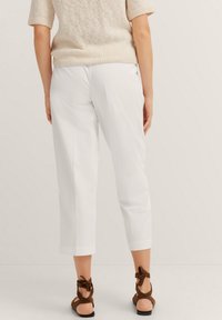 White cropped trousers with a smooth texture, featuring a straight cut. Paired with brown heeled sandals with bow accents.