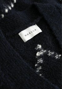 Granatowy sweter z dzianiny o fakturowanym splocie i białym nakrapianym wzorze, z wszytą metką oznaczoną "NOELLA".