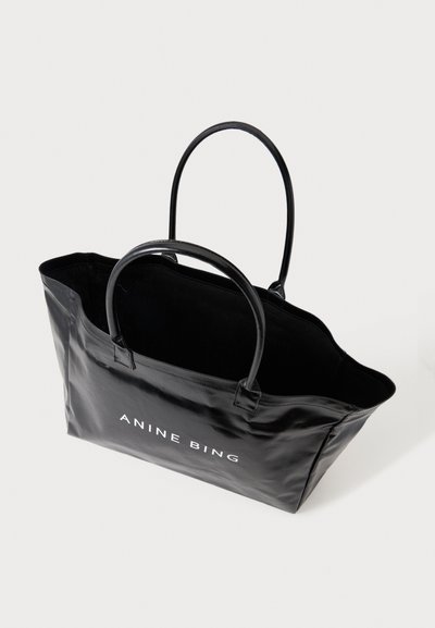 Sac cabas en cuir noir avec deux poignées et "ANINE BING" imprimé en blanc sur le devant, présenté sur un fond uni.
