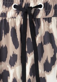 Tissu beige et noir à imprimé animalier avec un cordon noir passé dans des œillets argentés à la taille, noué d'un simple nœud.