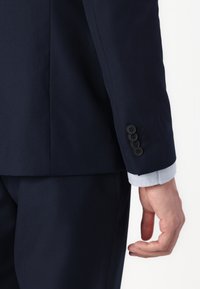 Navy blue suit jacket with a slim fit, featuring four black buttons on the cuff and a light blue shirt cuff peeking from underneath.