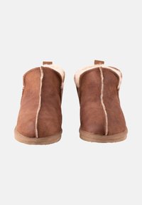 Chaussons en daim marron avec un intérieur doux et moelleux, une texture lisse, des coutures apparentes et une petite languette à l'arrière pour un enfilage facile.