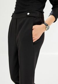Čierne elegantné nohavice s bočnými vreckami, s hladkým povrchom, plochým predným dielom a gombíkovým detailom na páse.