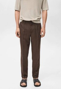 Pantalon marron sur mesure en tissu léger, avec une coupe droite et des poches latérales, assorti à des sandales plates noires.