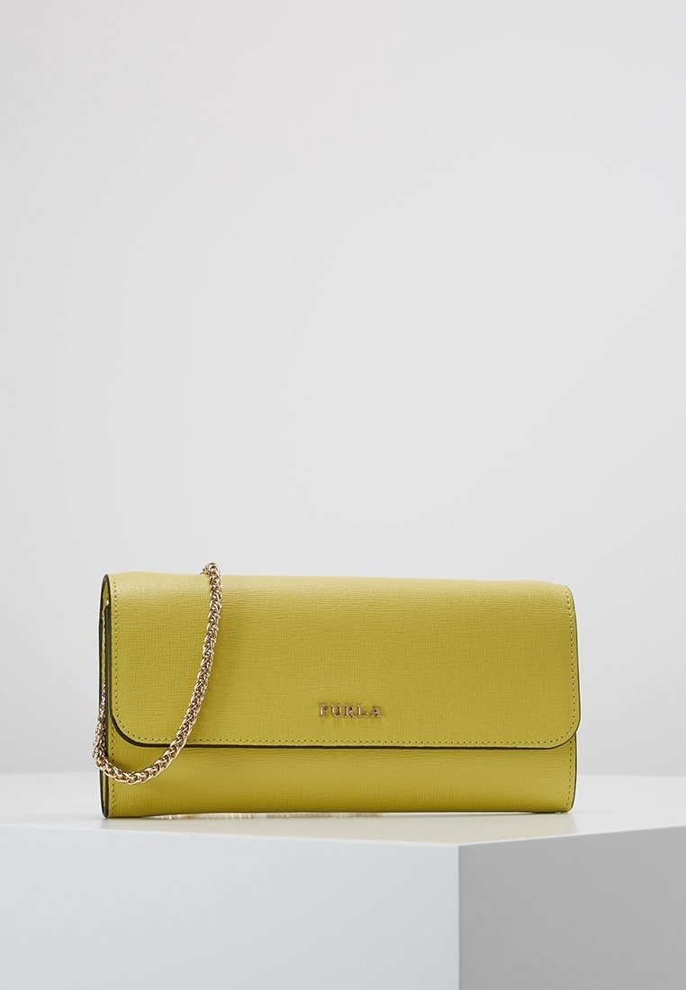 Pochette rectangulaire jaune Furla avec chaîne dorée, exposée sur un socle blanc sur fond gris.