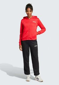 Red zip-up hoodie with a front pocket and white Adidas logo. Paired with black sweatpants featuring smaller white logo. Smooth fabric texture.