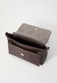 Brązowa skórzana torebka o fakturze krokodyla, z gładkim szarym wnętrzem, złotymi okuciami oraz klapą zamykaną na zatrzask.