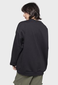 Crni oversized dukserica s okruglim izrezom, rebrastim manžetama i rubom. Mekani materijal, spuštena ramena i minimalno šivanje na leđima.