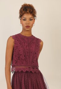 Burgunderfarbenes Spitzenkleid mit gewelltem Ausschnitt und detaillierten Blumenmustern. Durchsichtiger Rock mit Punkten, geschichteter Gestaltung und zartem Saum.