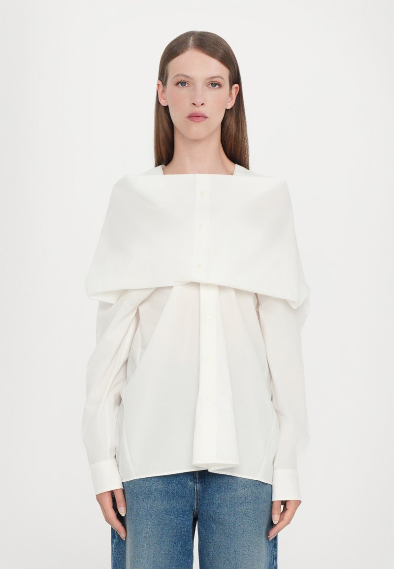 Witte blouse met oversized mouwen, die over de schouders valt, met een klassieke kraag en rechte zoom, gecombineerd met hooggewaadde blauwe jeans.