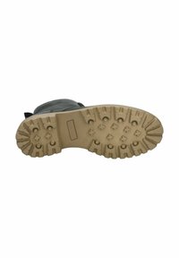 Semelle en caoutchouc avec des crampons profonds, de couleur beige, et motifs surélevés pour l'adhérence ; matériau supérieur gris partiellement visible en haut.