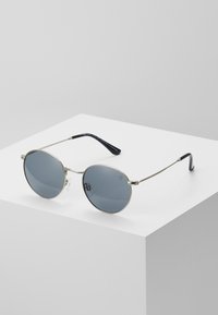 Ochelari de soare rotunzi cu lentile întunecate, cadru din metal argintiu și brațe din plastic negru. Prezintă un design minimalist și pernuțe nazale transparente.