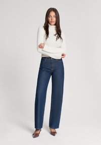 Ciemnoniebieskie dżinsy o wysokim stanie i prostym kroju, zestawione z dopasowanym białym golfem. Dżinsy mają subtelne detale przeszycia.