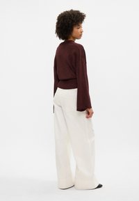 Suéter bordeaux com mangas largas e bainha canelada, combinado com calças brancas de pernas largas. Textura suave com ligeiro brilho.