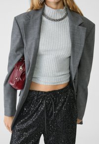 Grå skræddersyet blazer over en rippet lys grå cropped top, parret med sorte paljetbukser. Accessoriseret med en lille bordeaux håndtaske.