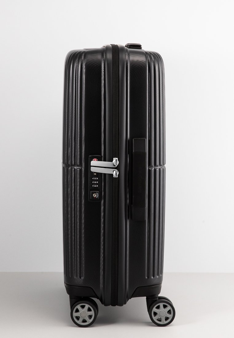 Black hard-shell suitcase with textured surface, combination lock, silver hardware, and four wheels for mobility.