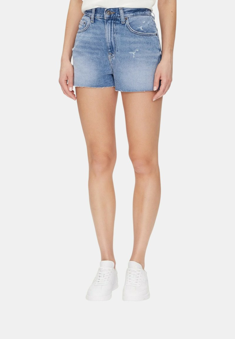 Shorts in denim di color azzurro chiaro con finitura invecchiata, orlo sfilacciato e design aderente. Indossati con sneakers bianche su uno sfondo semplice.
